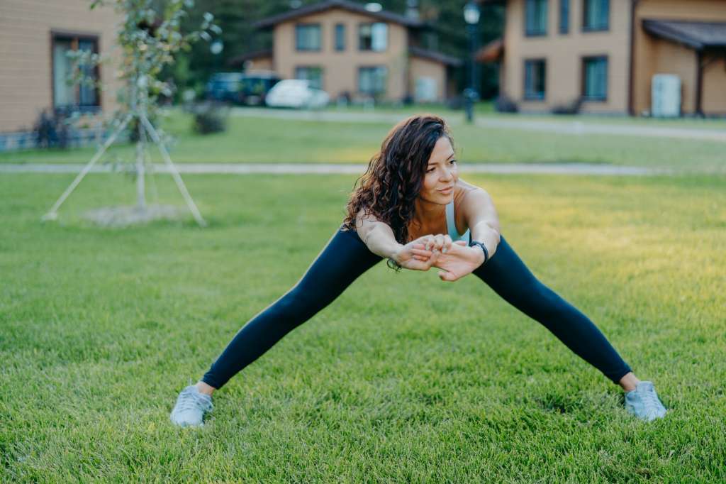 Athletic woman demonstrates her flexibility, stretches outdoors, does exercises early in morning